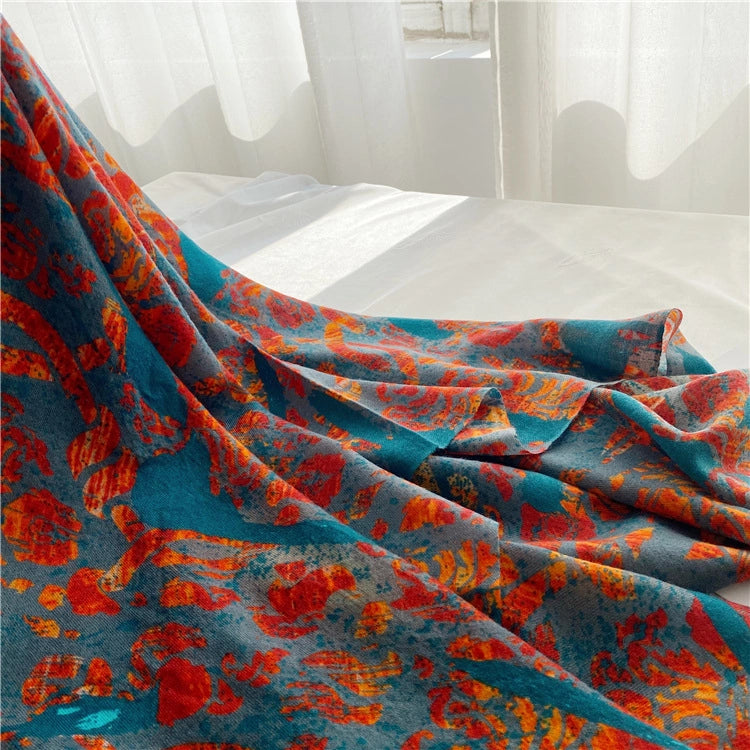 Oversized peacock print wool wrap draped in flowing folds across a white bed