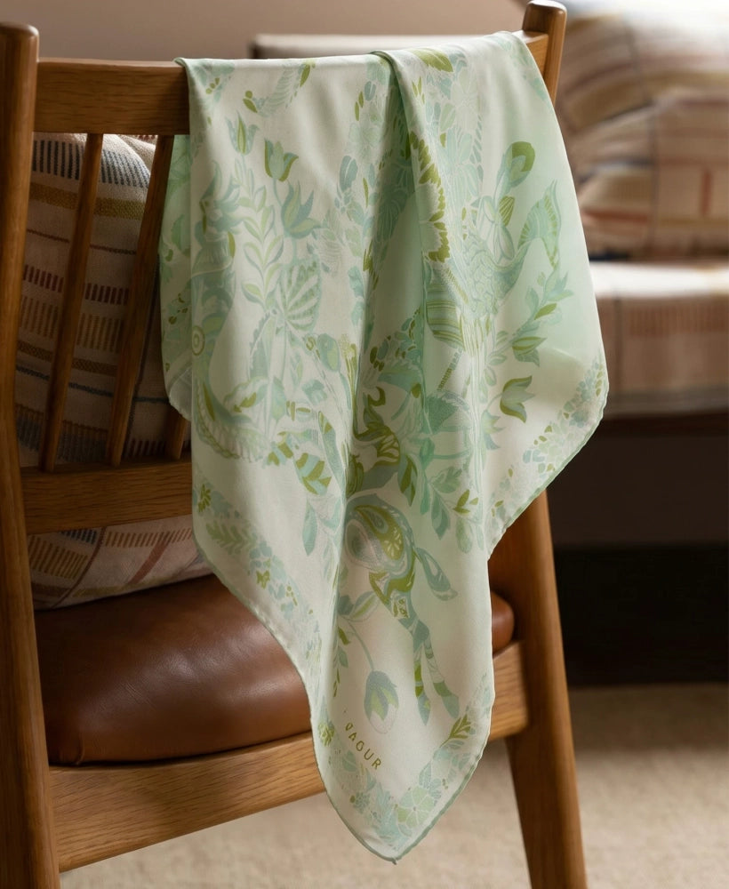 Tender green mulberry silk square scarf with elephant and floral print draped over a wooden chair