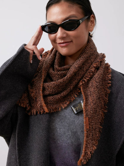 Terracotta cashmere triangle scarf wrapped around the neck, with layered folds and one long end over a charcoal sweater.