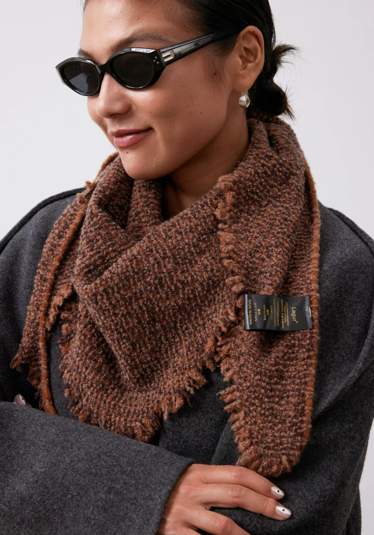 Side view of a model wearing a terracotta cashmere triangle scarf, showing layered knit folds and fringed edges.
