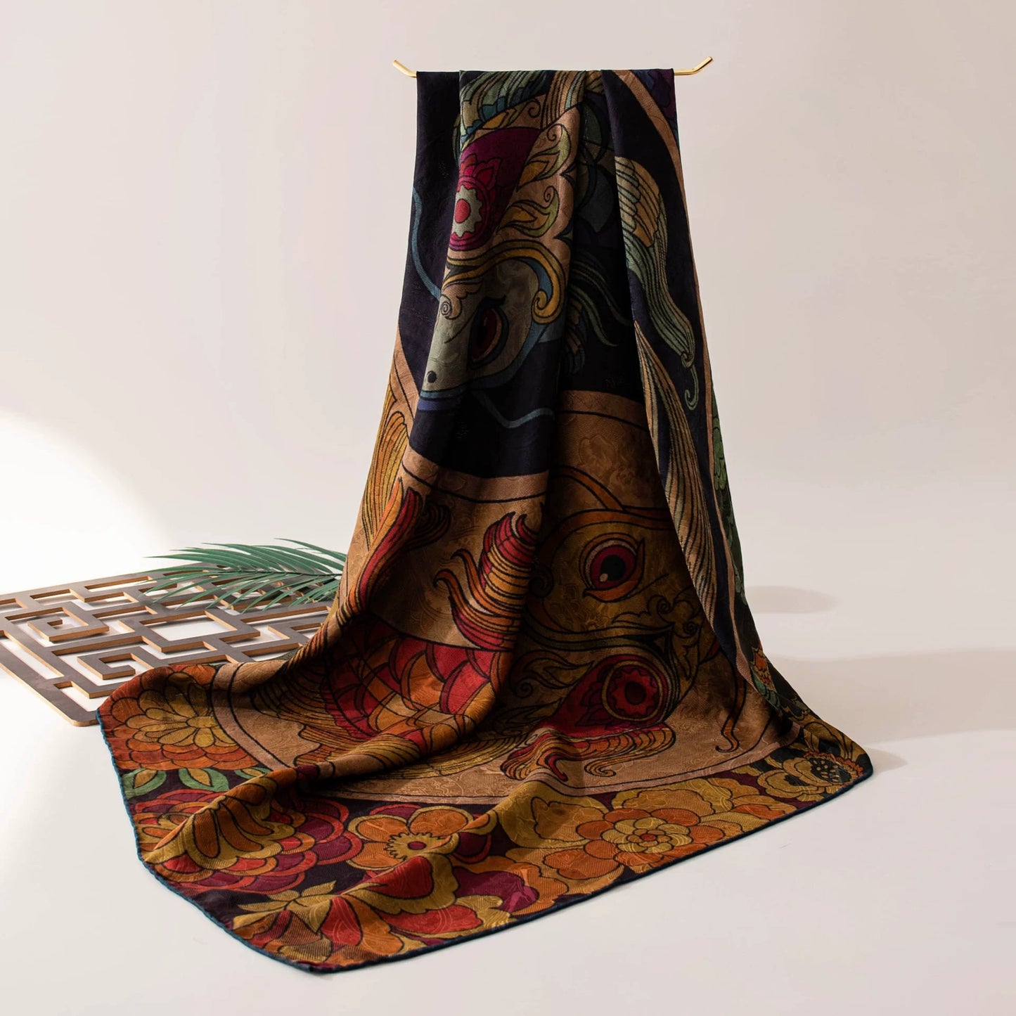 Twin fish Xiangyun silk scarf draped on a table, showing its dark floral border and lustrous finish