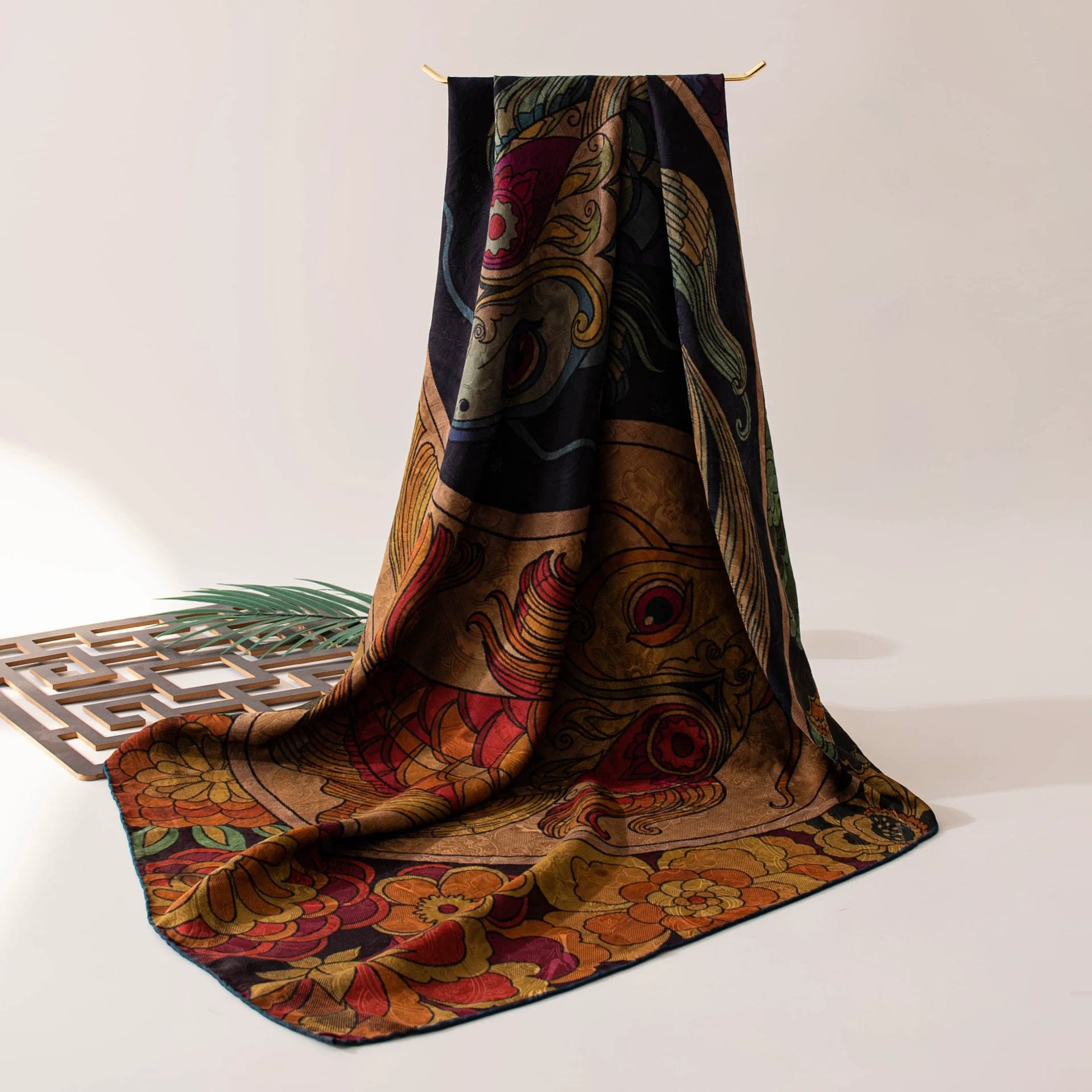 Twin fish Xiangyun silk scarf draped on a table, showing its dark floral border and lustrous finish