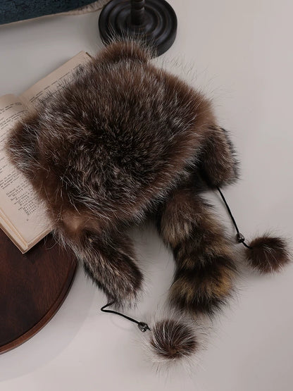 Flat lay of a brown-grey fur trapper hat with a fluffy crown, ear flaps, a ringed tail and pom-pom drawstrings.