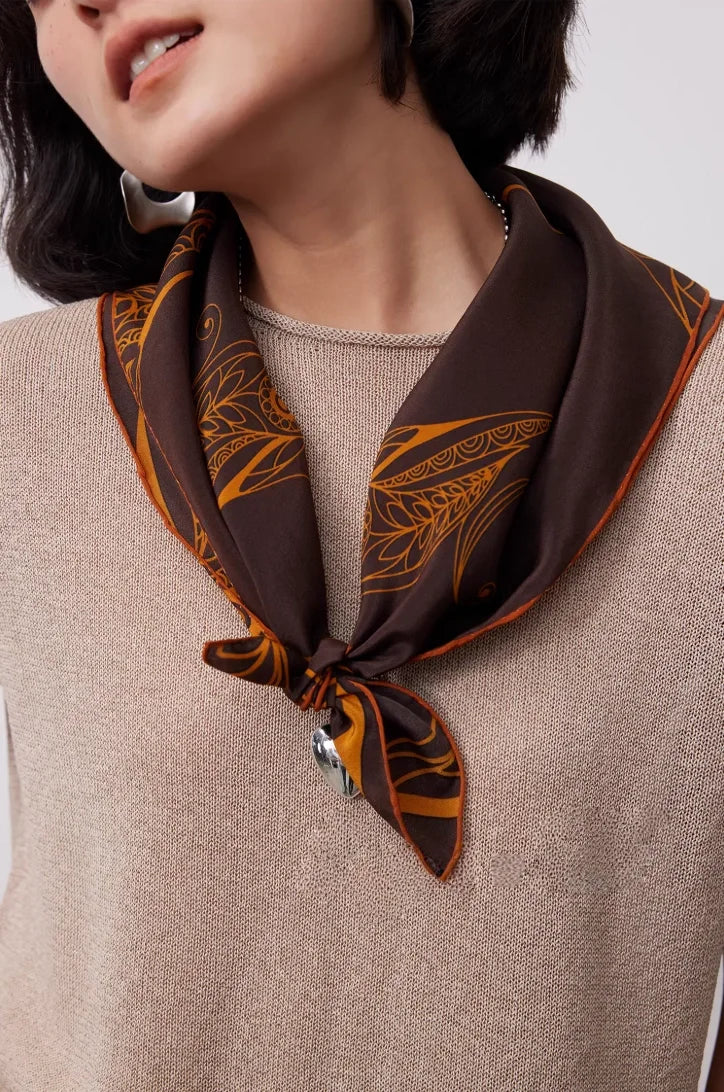 Close-up of brown 100% mulberry silk square scarf tied around the neck with elegant gold and paisley details.