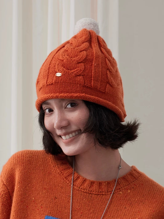 Vintage cable knit wool beanie in orange with a cream pom pom, paired with a matching sweater.