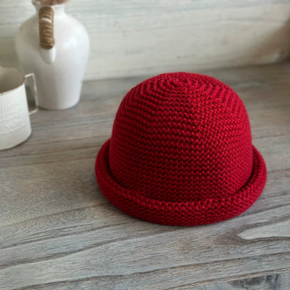 Vintage red wool blend knit beanie with a rounded dome crown and rolled brim on a wooden table