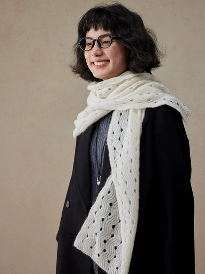 Angled view of a cream white cashmere scarf, showing its wave pointelle knit and drape over a black coat.