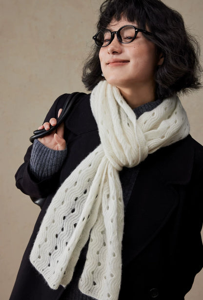 Cream white cashmere scarf tied in a loose front knot over a black coat, showing its openwork texture.