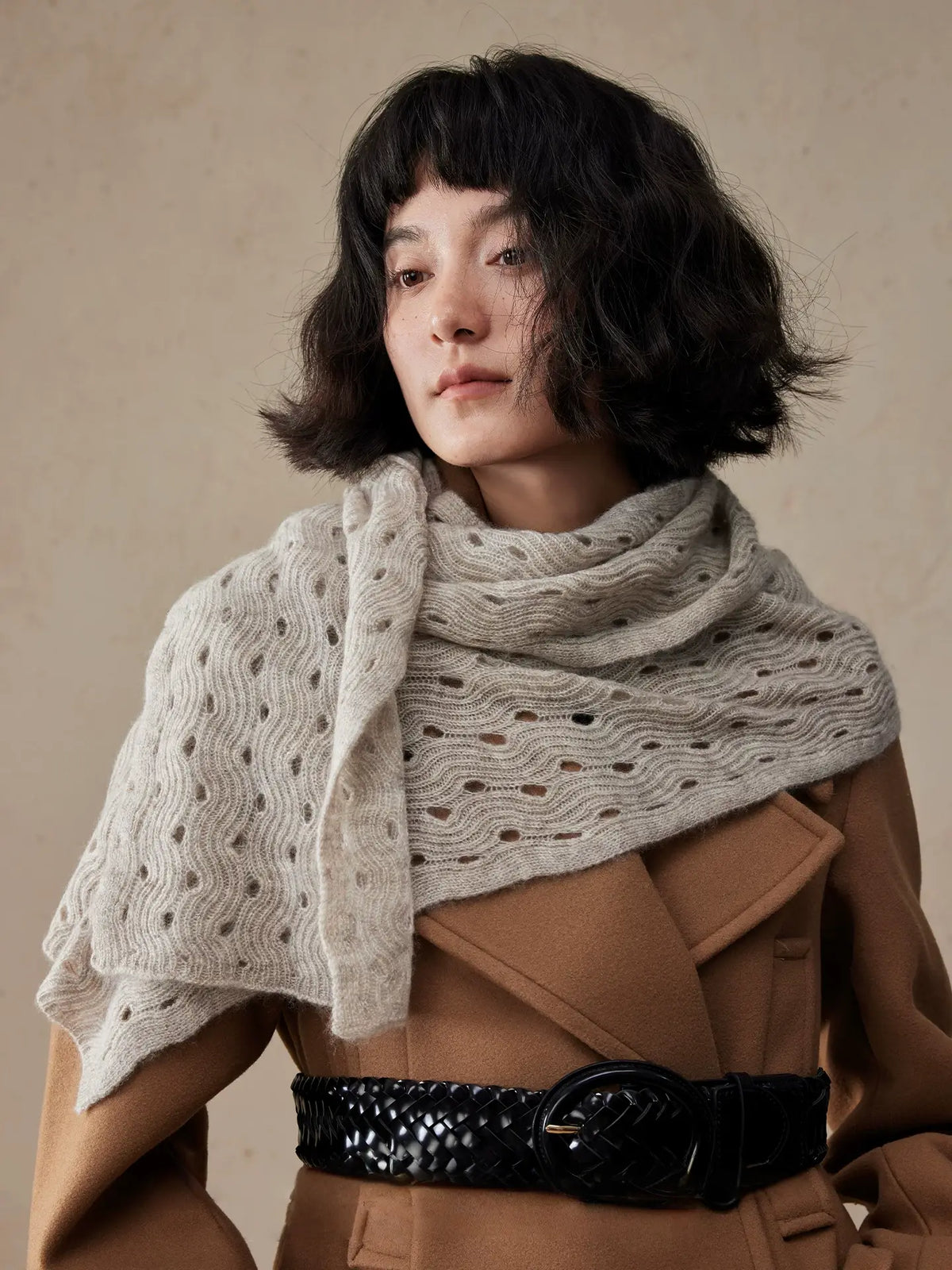 Light khaki wave pointelle cashmere scarf draped across the shoulders over a belted camel coat.