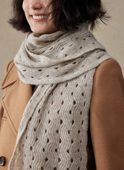 Close-up of a light khaki cashmere scarf over a camel coat, showing the wave pointelle texture along its hanging ends.