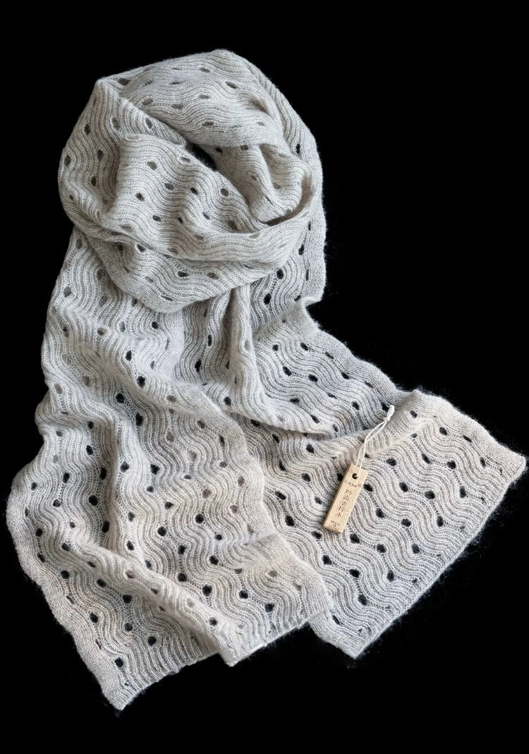 Light khaki wave pointelle cashmere scarf loosely coiled on a black background, with both ends displayed.
