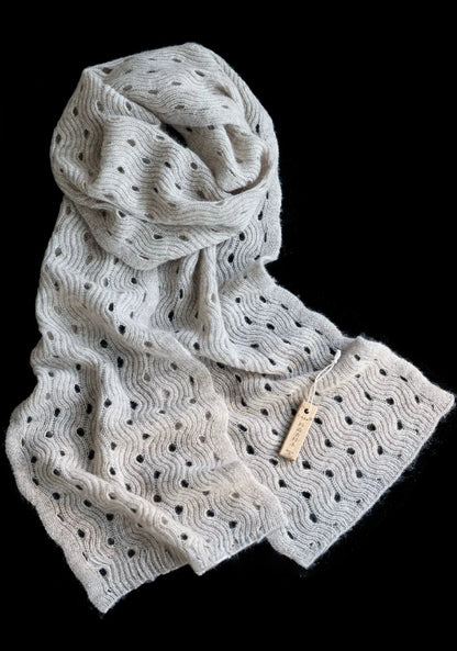 Light khaki wave pointelle cashmere scarf loosely coiled on a black background, with both ends displayed.
