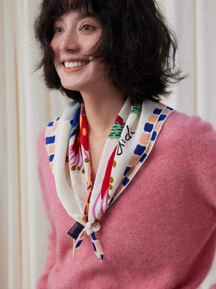 Woman wearing an ivory bird print mulberry silk scarf loosely knotted over a pink sweater
