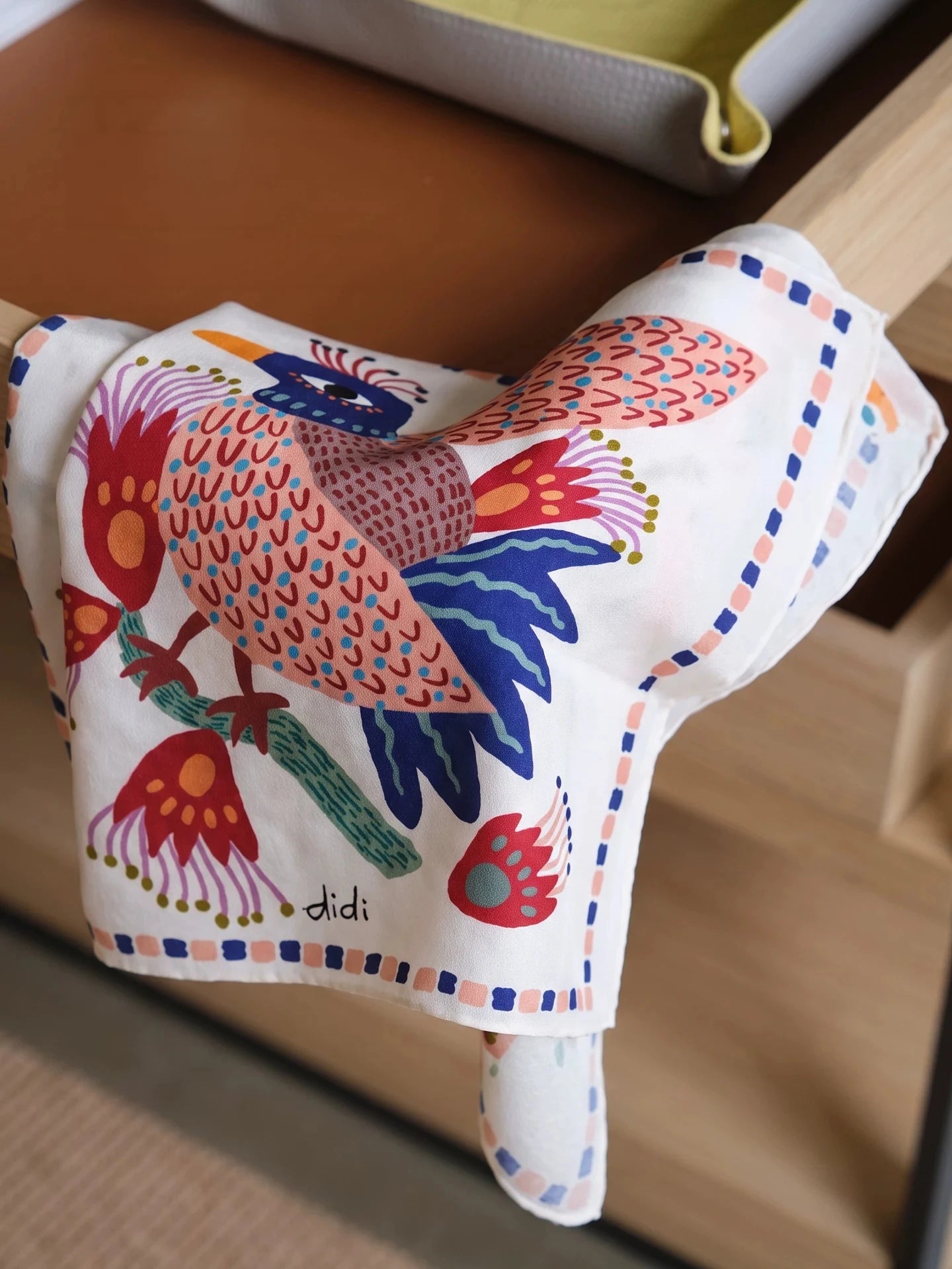 Colorful bird print mulberry silk scarf draped over a wooden table to show its soft sheen