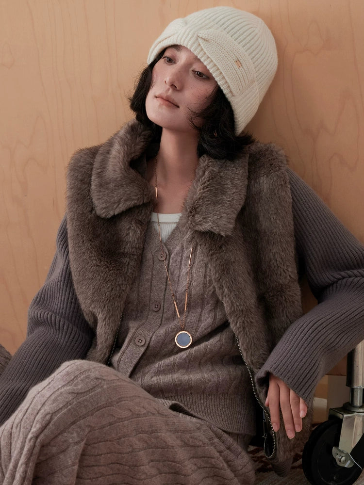 Seated model styling a white wool bow beanie with brown knitwear and a textured vest.
