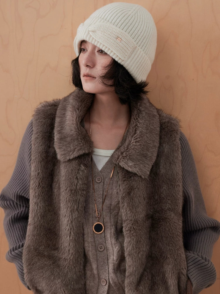 White wool bow beanie worn with a brown textured vest, showing the hat's rounded crown and ribbed knit.