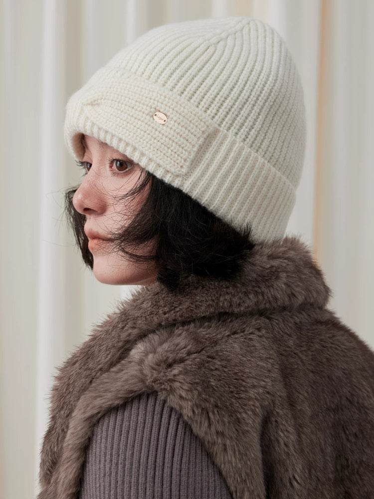 Side view of a white wool bow beanie on a model, showing the ribbed crown and folded cuff.