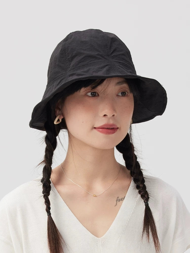 Front view of a woman wearing a black wide brim bucket hat, styled with twin braids and a white top.