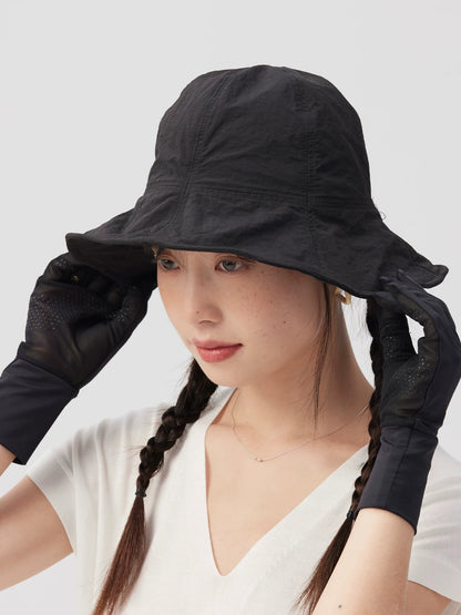 Woman holding both sides of a black bucket hat's wide brim with gloved hands.