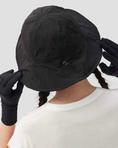Close-up rear view of a black bucket hat showing crown seams and a wide brim held with both hands.