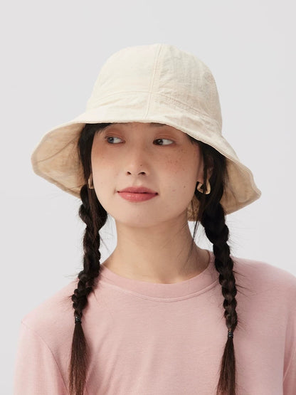 Front view of a woman wearing an ivory wide brim bucket hat with twin braids and a pink top.