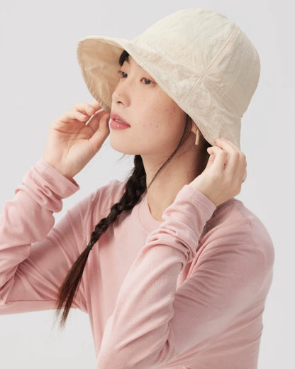 Side view of a woman wearing an ivory wide brim bucket hat with the front brim gently curved upward.