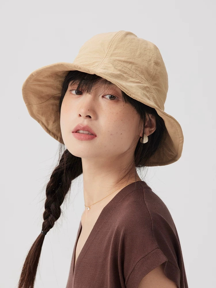 Three-quarter view of a woman wearing a khaki wide brim bucket hat with twin braids and a brown top.