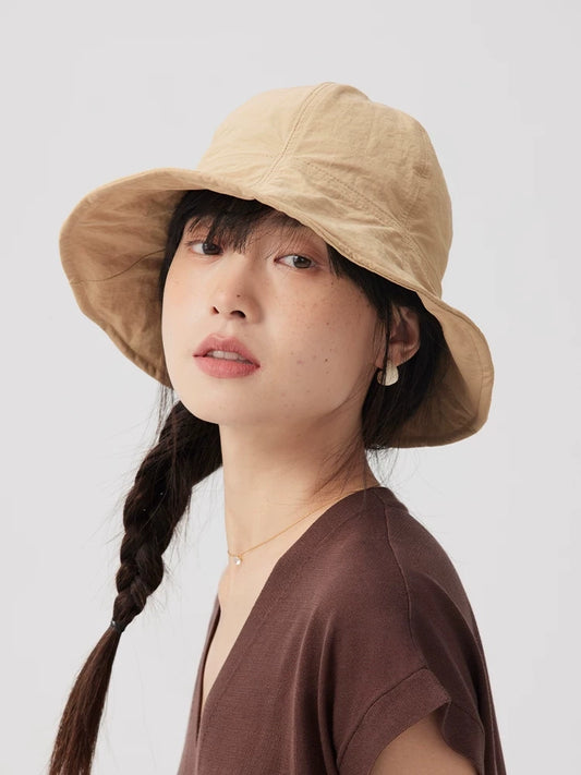 Three-quarter view of a woman wearing a khaki wide brim bucket hat with twin braids and a brown top.