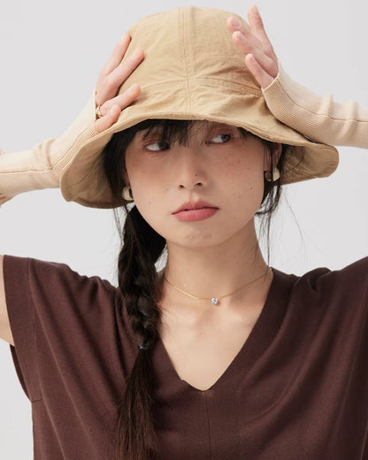 Woman wearing a khaki wide brim bucket hat with both hands resting on the rounded crown.