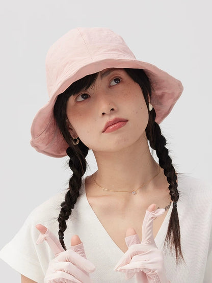 Front view of a woman wearing a pale pink wide brim bucket hat with twin braids and a white V-neck top.