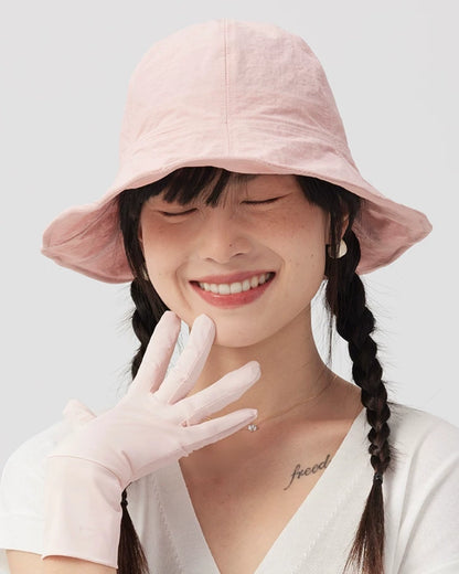 Woman smiling with her eyes closed in a pale pink wide brim bucket hat, with a gloved hand near her face.