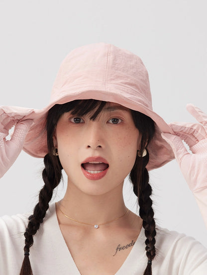 Front view of a woman holding both sides of a pale pink bucket hat's wide brim.