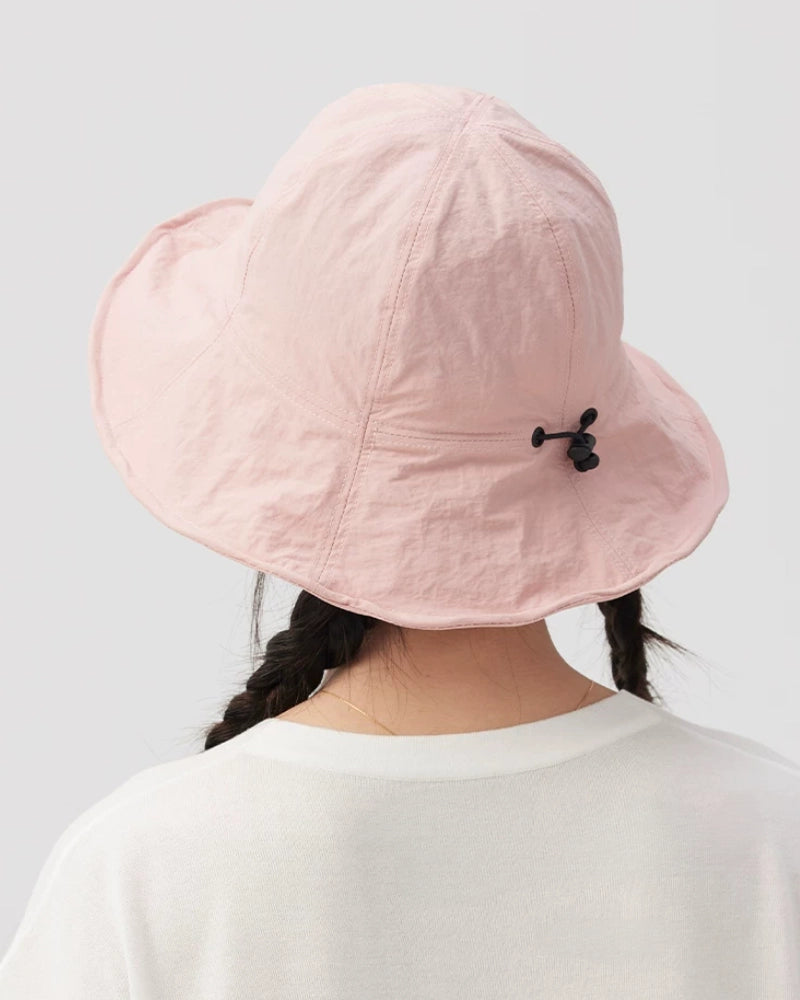 Rear view of a pale pink bucket hat showing the black drawstring toggle, rounded crown and wide brim.