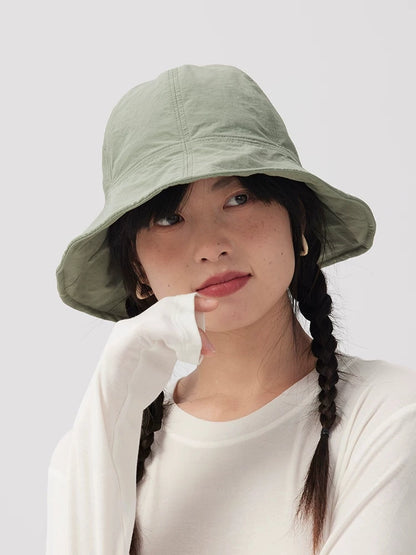 Woman wearing a sage green wide brim bucket hat with twin braids and one hand resting near her chin.