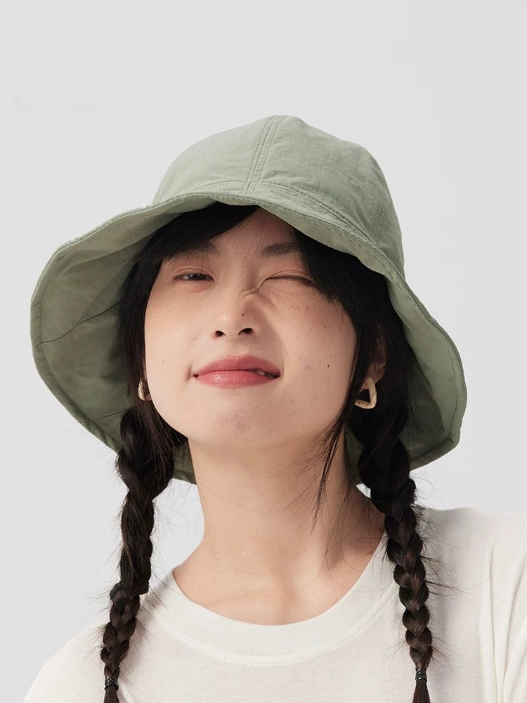 Front view of a woman wearing a sage green bucket hat, showing the wide brim and rounded crown.
