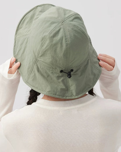 Close-up rear view of a sage green bucket hat showing crown seams, a black drawstring toggle and a curved brim.