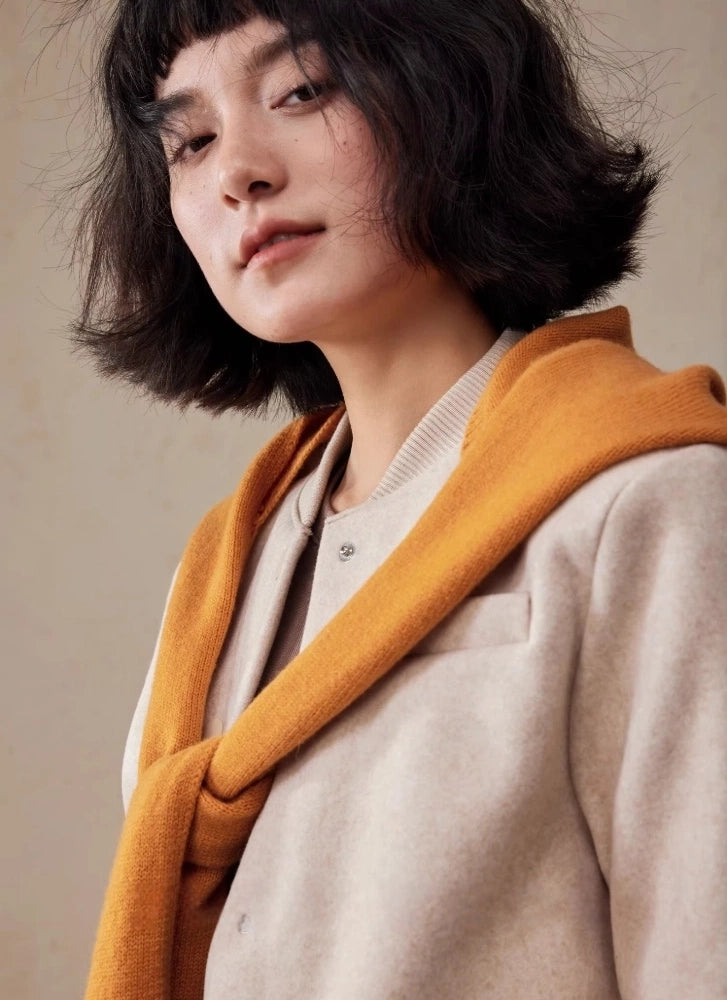 Woman styling a burnt orange wool hooded scarf over a beige blazer