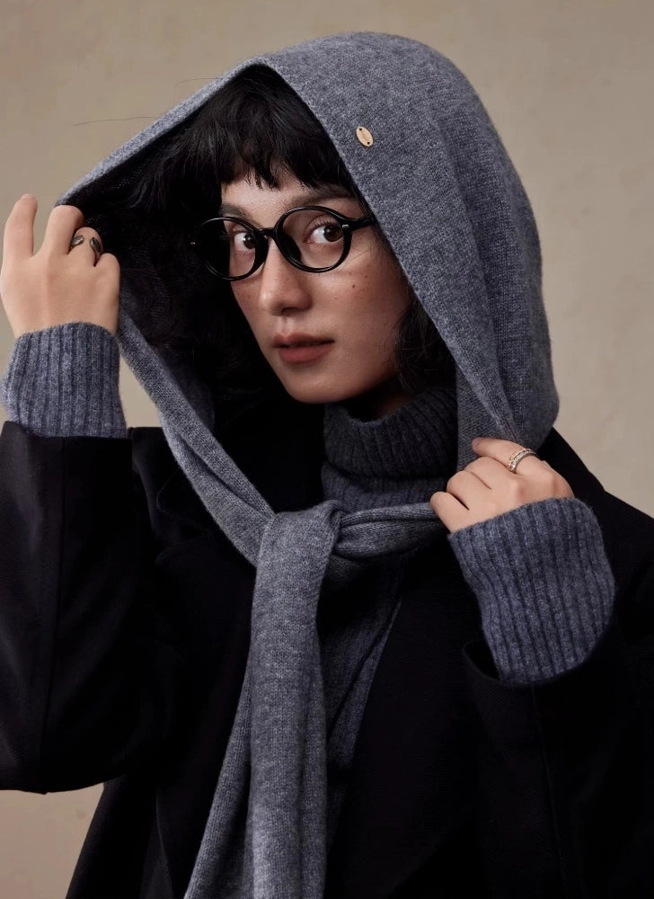 Woman adjusting a dark grey wool hooded scarf while wearing a black coat