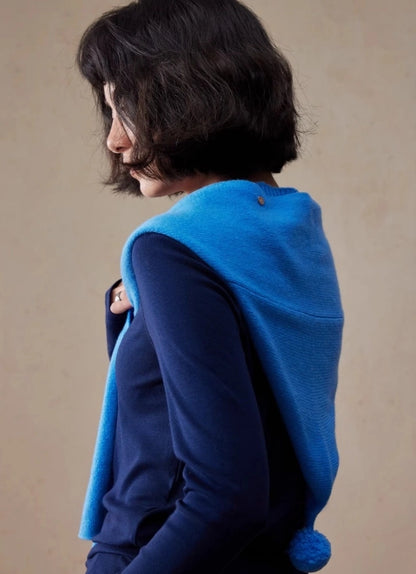 Side back view of royal blue wool hooded scarf draped over the shoulders with pom pom detail