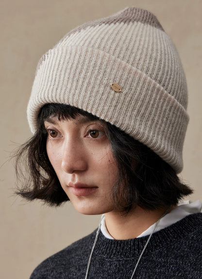 Close-up of a beige taupe two-tone wool beanie worn by a model, showing vertical ribbing and a folded cuff.