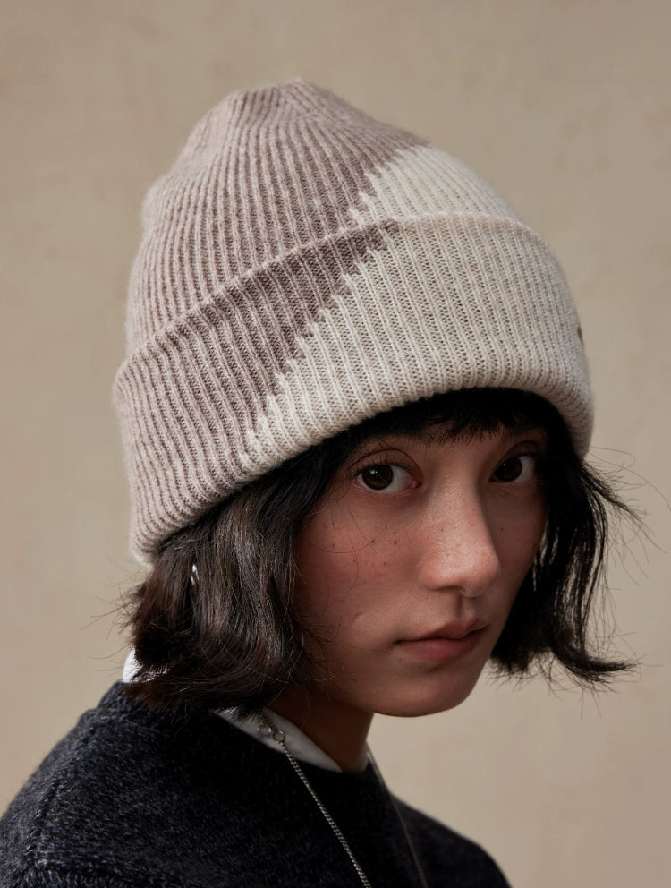 Angled front view of a beige taupe color block knit hat, highlighting its diagonal contrast and broad folded cuff.