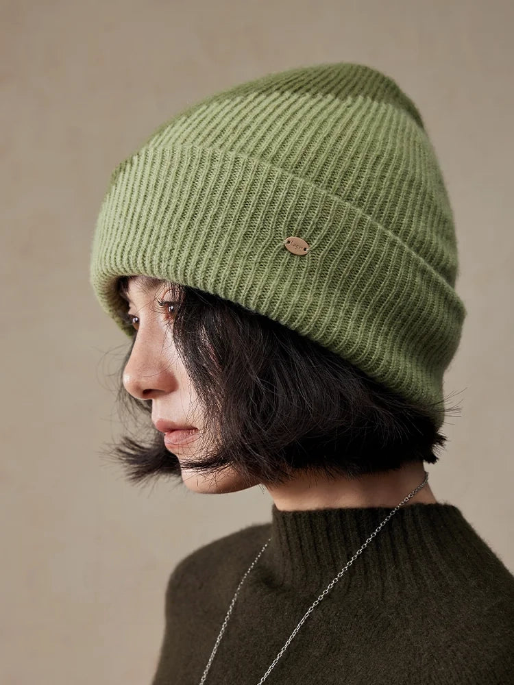 Left-facing profile of a model wearing a moss green wool cuff beanie with vertical ribbing and a gold-tone detail.