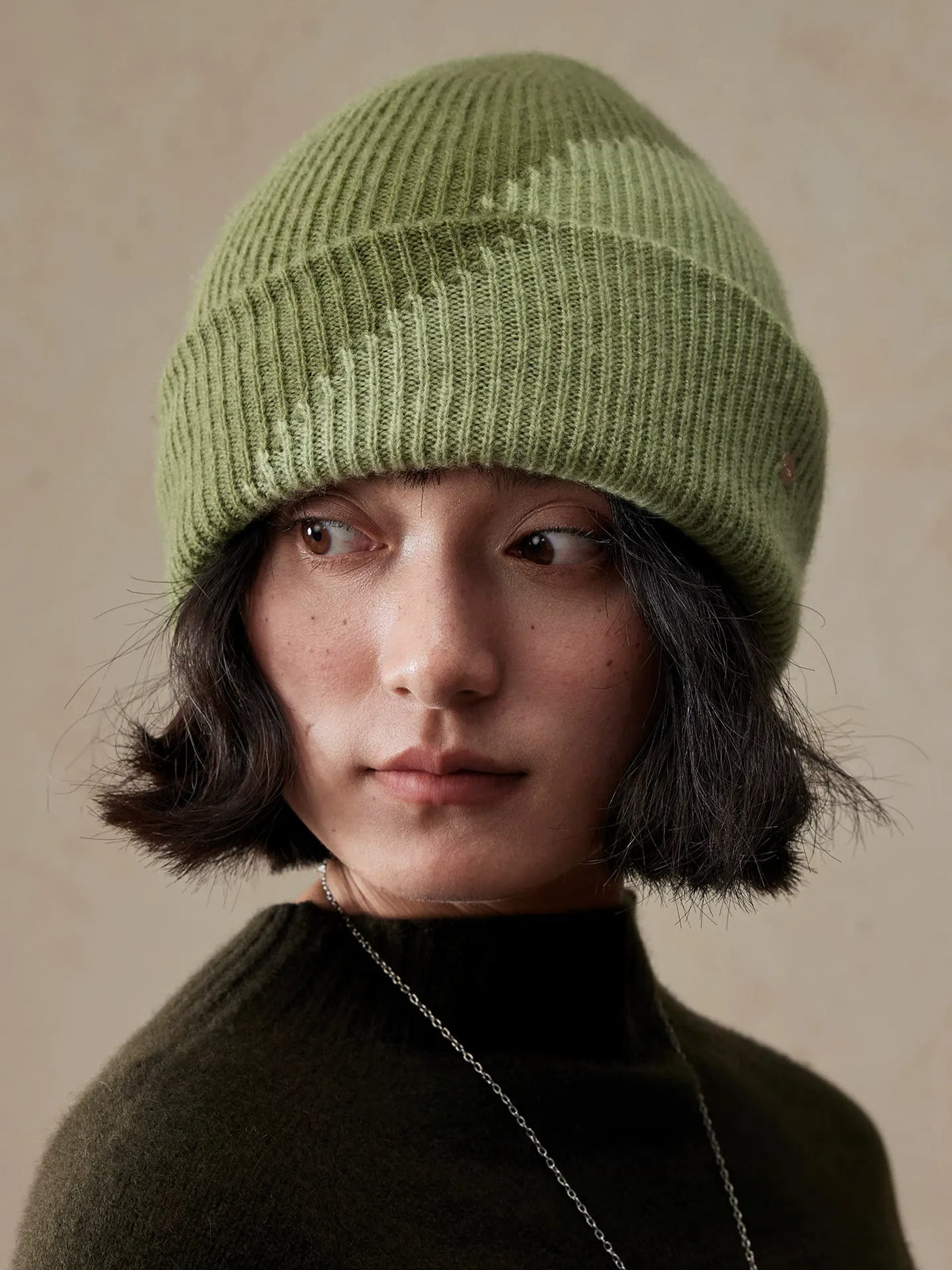 Front view of a moss green diagonal color block wool beanie worn by a model, showing the folded cuff and ribbed texture.