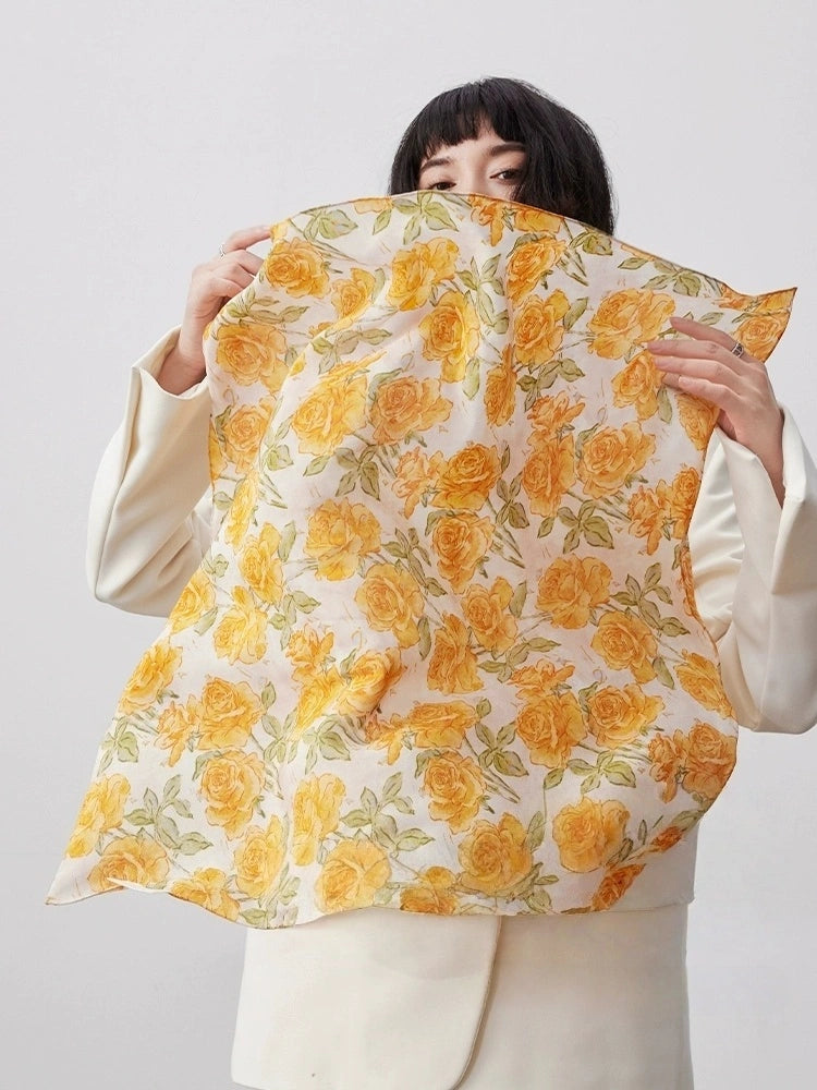 Elegant yellow rose print silk square scarf draped gracefully, emphasizing its smooth texture and timeless design.