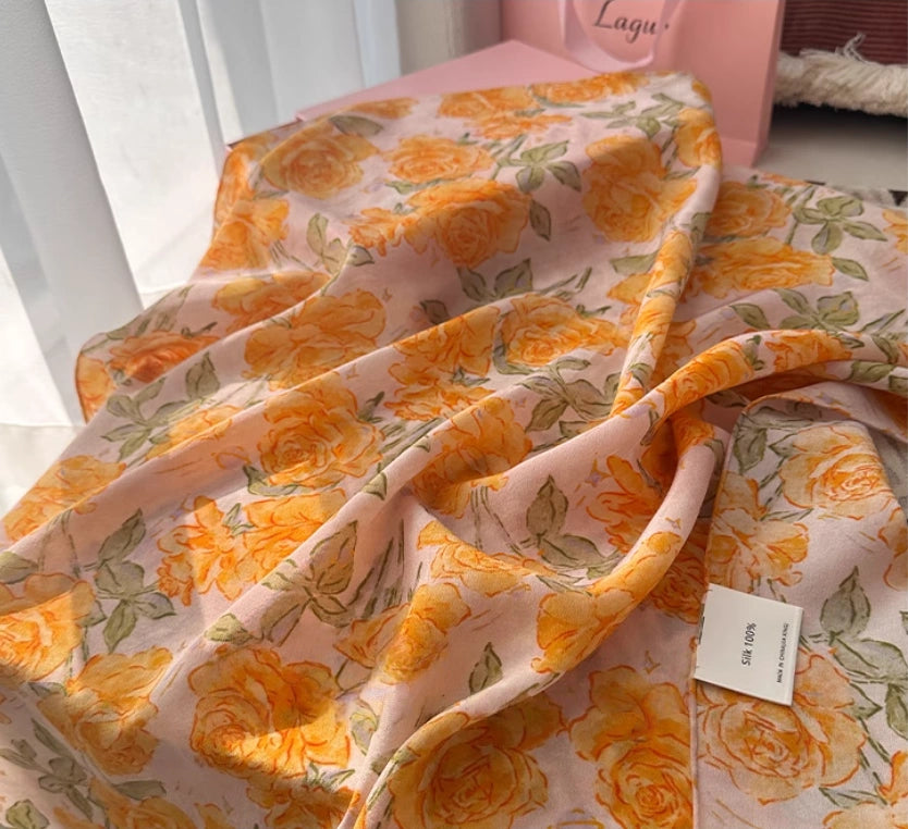 Flat lay of a yellow rose print silk square scarf, crafted from 100% mulberry silk, perfect for all-season wear.
