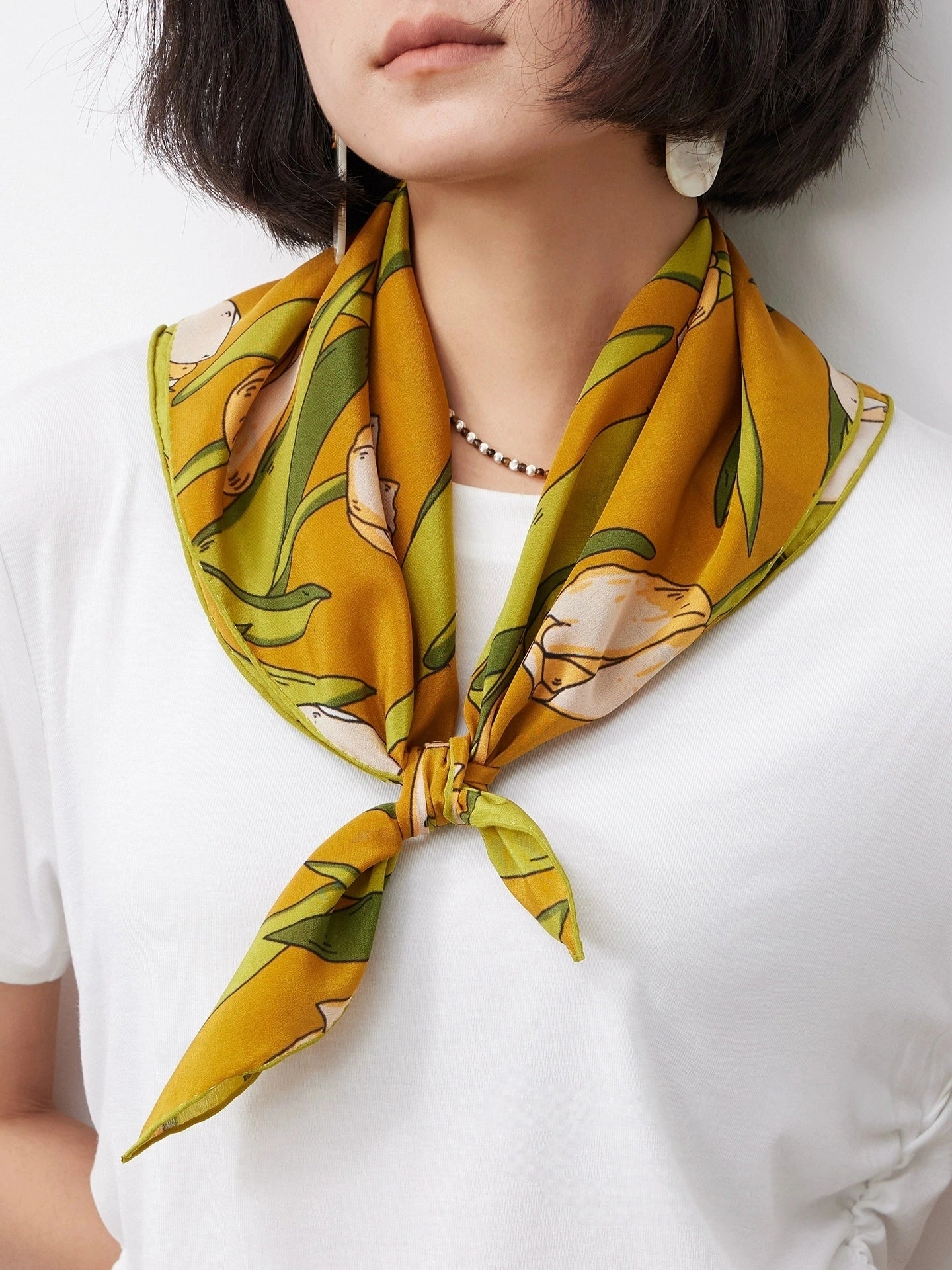 A yellow tulip floral print silk square scarf made from 100% mulberry silk is shown close-up as a neck scarf.