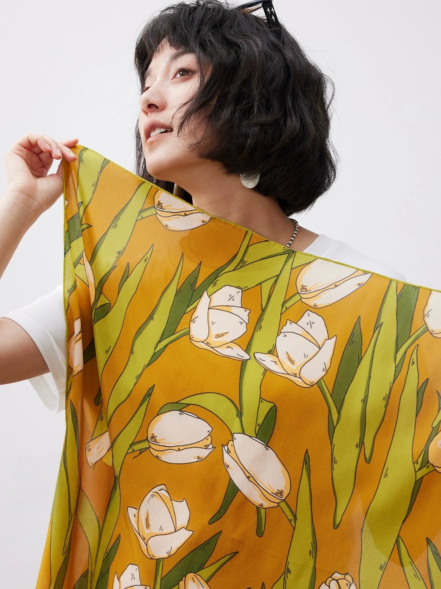 A model displays a close-up of a yellow tulip floral-print silk scarf.